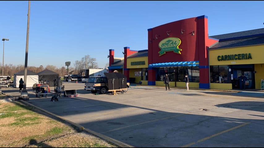 A film crew and production van set up with cameras and gear outside the vibrant Ideal Market—its "Carniceria" sign visible—creates the feel of a live movie shoot at Universal Studios, immersing guests in an authentic behind-the-scenes National Treasure experience.