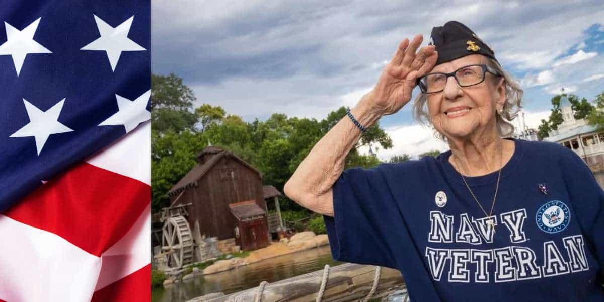 An elderly woman wearing a "Navy Veteran" shirt and cap salutes as she stands outdoors, embraced by a rustic scene of trees and a wooden building. To her left, an American flag waves proudly. It's a moment reminiscent of when Disney honors veterans with heartfelt tributes.