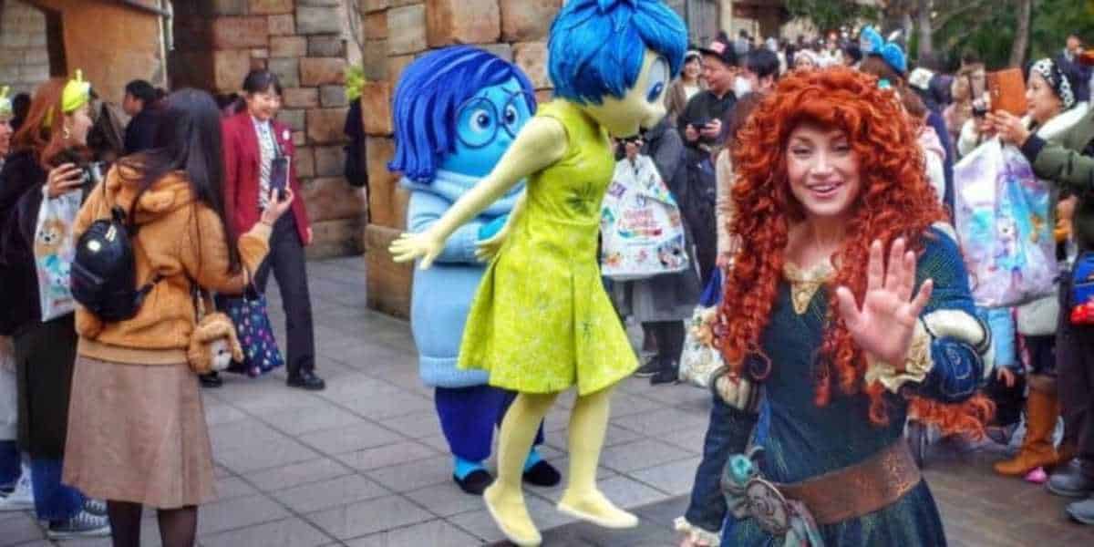 Joy, Sadness, and Merida at Disney Park among crowd of Guests