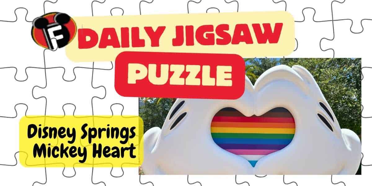 A colorful jigsaw puzzle design features the text "Daily Jigsaw Puzzle" in bold red and white letters on an orange background. Below is "Disney Springs Mickey Heart" written in black on a yellow background. An image of a Mickey Mouse heart with a rainbow center is displayed.