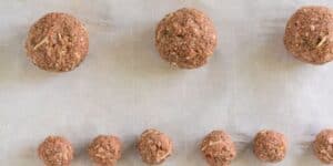Nine uncooked meatballs of varying sizes are arranged on a parchment paper-lined baking sheet. The larger meatballs are at the top, while the smaller ones are at the bottom, showcasing a progression from largest to smallest.