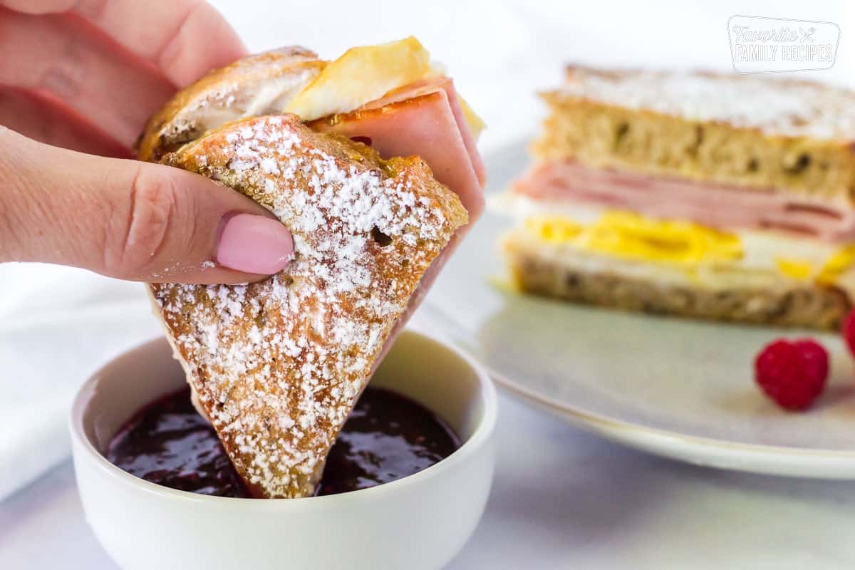 This Monte Cristo breakfast sandwich is a delicious twist on a classic! Sweet and savory meet together in this easy-to-make, decadent breakfast sandwich. Half of Breakfast Monte Cristo Sandwich dipping in jam.
