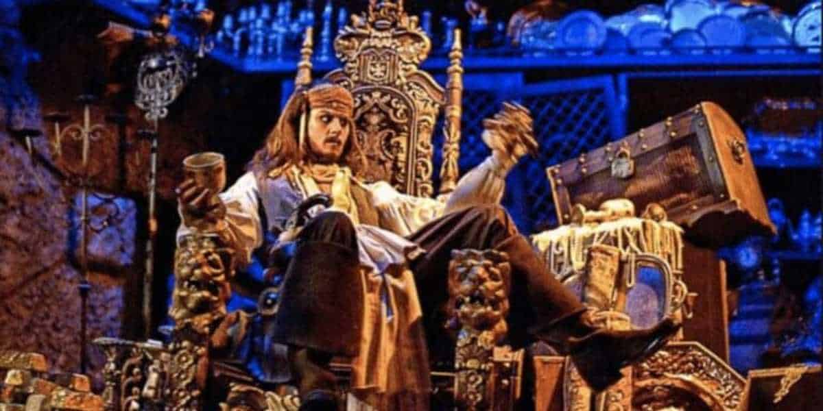 A person in pirate attire sits on an ornate throne surrounded by treasures and gold. They hold a goblet in one hand and a small item in the other. The scene is dimly lit with a blue hue, enhancing the dramatic, adventurous atmosphere.