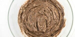 A glass bowl containing a mixture of brown and beige batter with a thick, swirling texture. The mixture has a marbled appearance, suggesting it could be a chocolate or mocha-flavored preparation for baking. The bowl sits on a white surface.