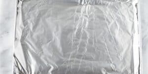 A baking sheet covered with crinkled aluminum foil, placed on a white surface. The edges of the foil are folded over the sides of the baking sheet, suggesting it is prepared for use in cooking or baking a jalapeño cheese stuffed pretzel recipe inspired by Disney.