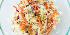 A clear glass bowl filled with a fresh coleslaw salad featuring shredded cabbage, julienned carrots, and slices of purple cabbage. The vibrant colors and crisp textures of the vegetables are visible, making the dish appear fresh and appetizing—a Satu'li Bowls recipe inspired by Pandora - World of Avatar.