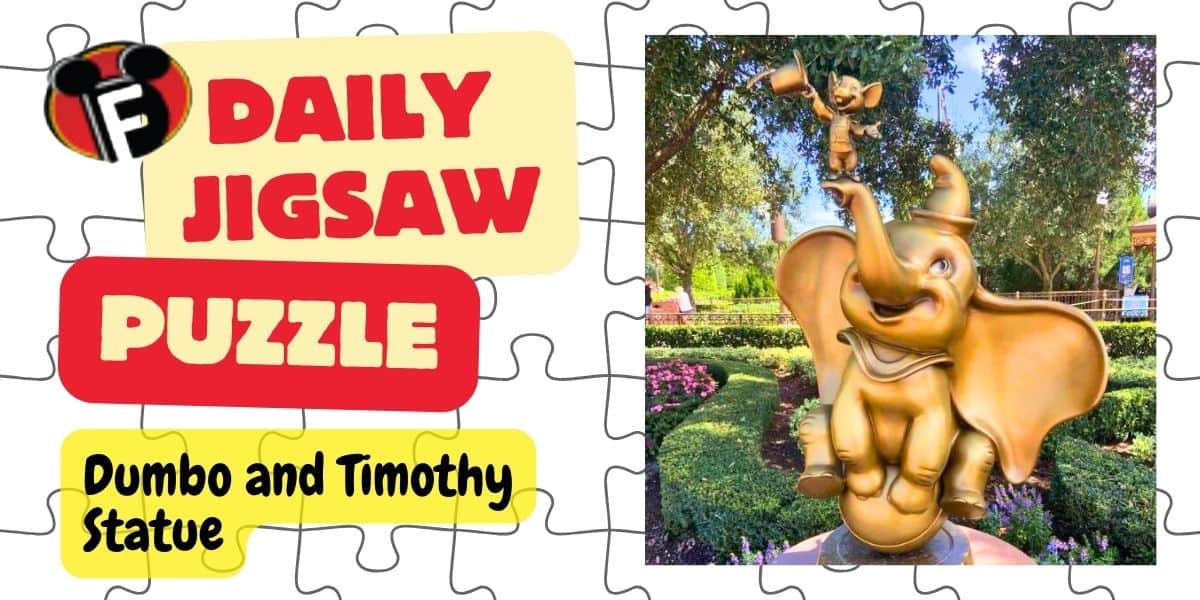 Advertising graphic for a daily Disney Jigsaw Puzzle featuring a statue of Dumbo and Timothy Mouse. Dumbo, the elephant, is balanced on a ball with Timothy on his hat. The statue is surrounded by a garden with flowers and trees in the background.