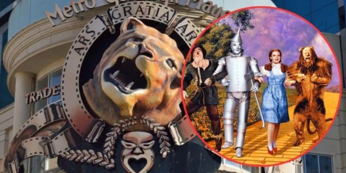 An emblem depicting a roaring lion for "Metro Goldwyn Mayer" is displayed on a building. Overlaid on the emblem is a scene from "The Wizard of Oz" with the Scarecrow, Tin Man, Dorothy, and the Cowardly Lion walking down the yellow brick road.