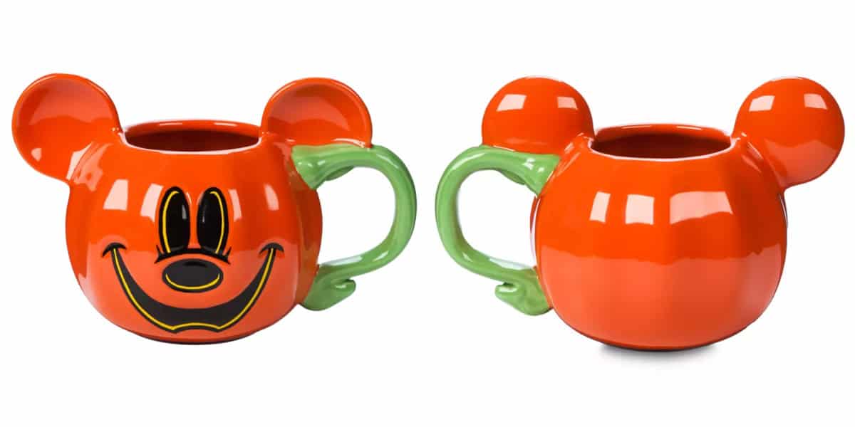 Two ceramic mugs with Mickey Mouse face designs. The mugs are orange with green handles shaped like tails and have Mickey's face on one side. Ears protrude from the top, mimicking a pumpkin shape.