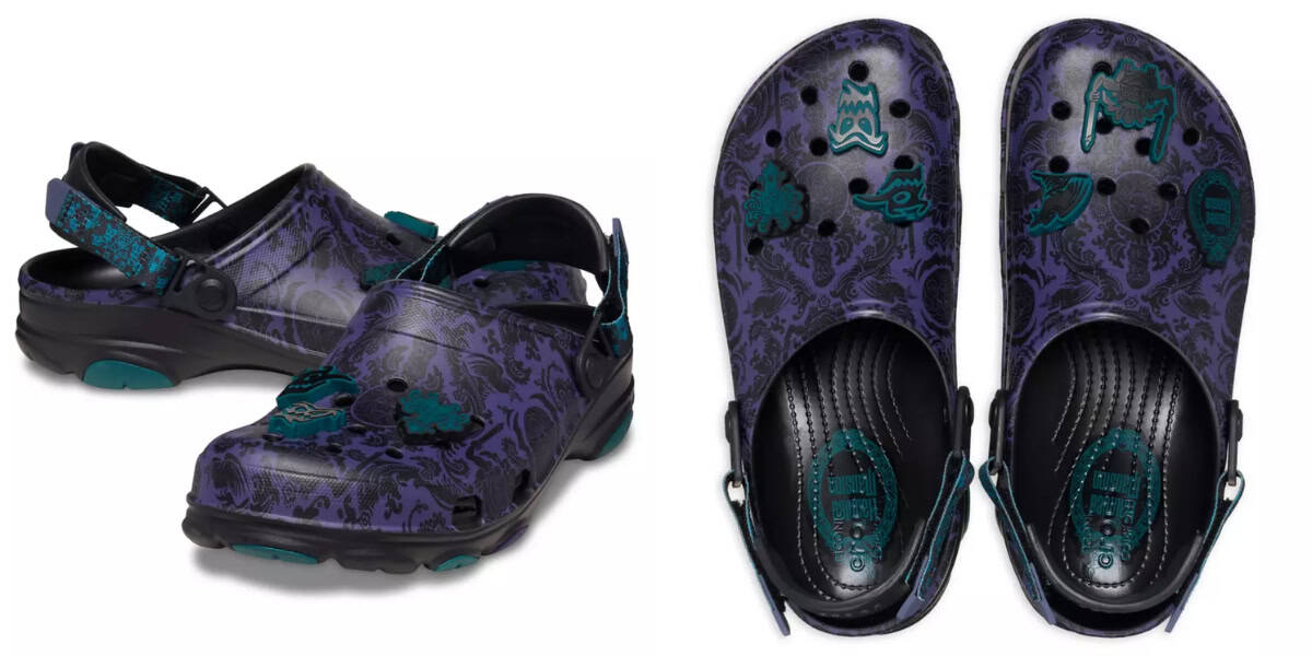 A pair of purple Crocs with a black damask pattern. The shoes feature green decorative charms on top, including spooky icons like a ghost, bat, and haunted house. The heel straps are adjustable, and the undersides are visible in one of the views.