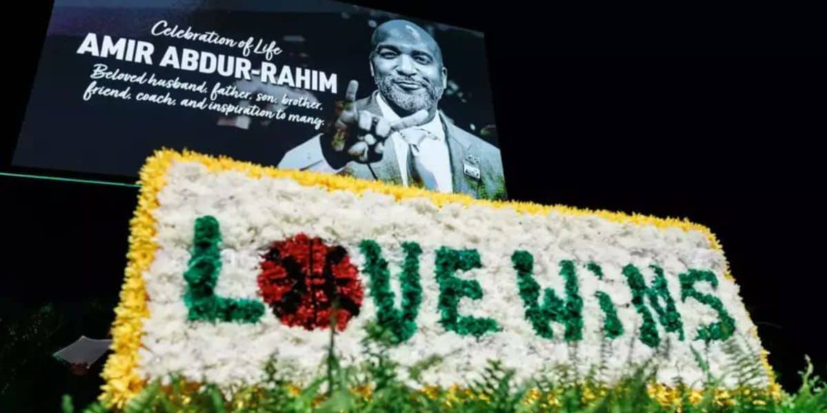 A tribute event features a large banner with a grayscale image of a smiling man, labeled "Amir Abdur-Rahim." Below, a floral arrangement spells "LOVE WINS" in red and green flowers with a yellow border.
