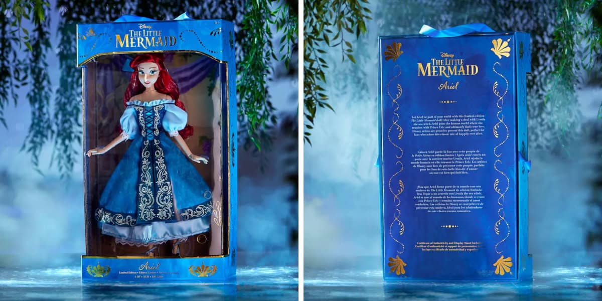 The image shows a "The Little Mermaid" Ariel doll in its box. The packaging is blue with ornate designs and text in gold. The doll features red hair and a detailed blue dress with white accents. The background setting is misty and nature-themed.