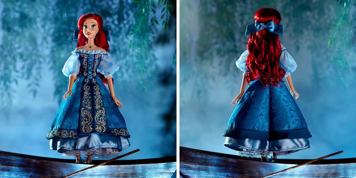 A doll with long red hair wears a blue dress with intricate gold embroidery. The doll is shown from the front and back, standing on a wooden surface. The background is misty with green foliage.