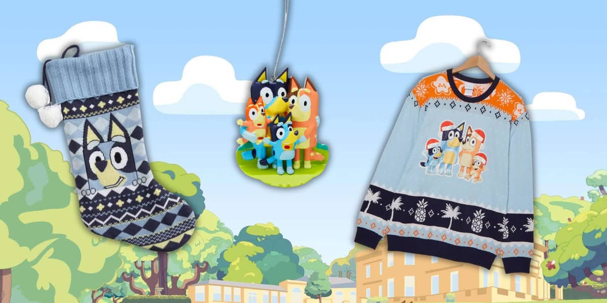A festive display featuring a pastel blue Christmas stocking with a dog design, a hanging ornament with cartoon dog characters, and a holiday sweater with a similar design, set against a cartoon backdrop of trees and buildings.