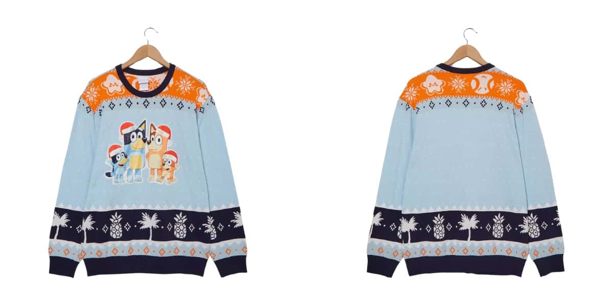 Front and back view of a light blue holiday sweater on a hanger. The front features cartoon dogs in Santa hats, with orange, white, and navy snowflake and festive patterns along the collar and hem. The back shows continued patterns.