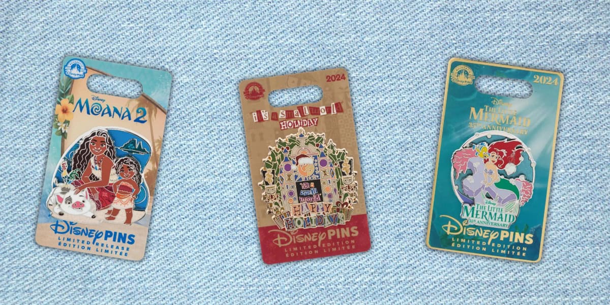 Three Disney collectible pins on a light blue textured surface. From left to right: a "Moana 2" design with Moana and Maui, a holiday pin with "A Very Merry Happy Holiday" text, and a "The Little Mermaid" design featuring Ariel and Ursula.