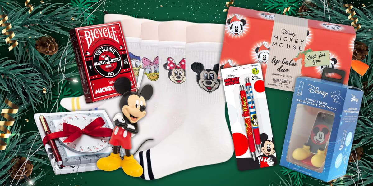 A festive assortment of Disney-themed gifts including Mickey Mouse playing cards, socks with character faces, a lip balm duo, pens, and a Mickey figurine, surrounded by pine branches and a green background with subtle star patterns.
