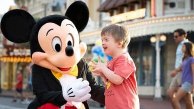 A child wearing a red Mickey Mouse shirt smiles excitedly while interacting with a person in a Mickey Mouse costume.