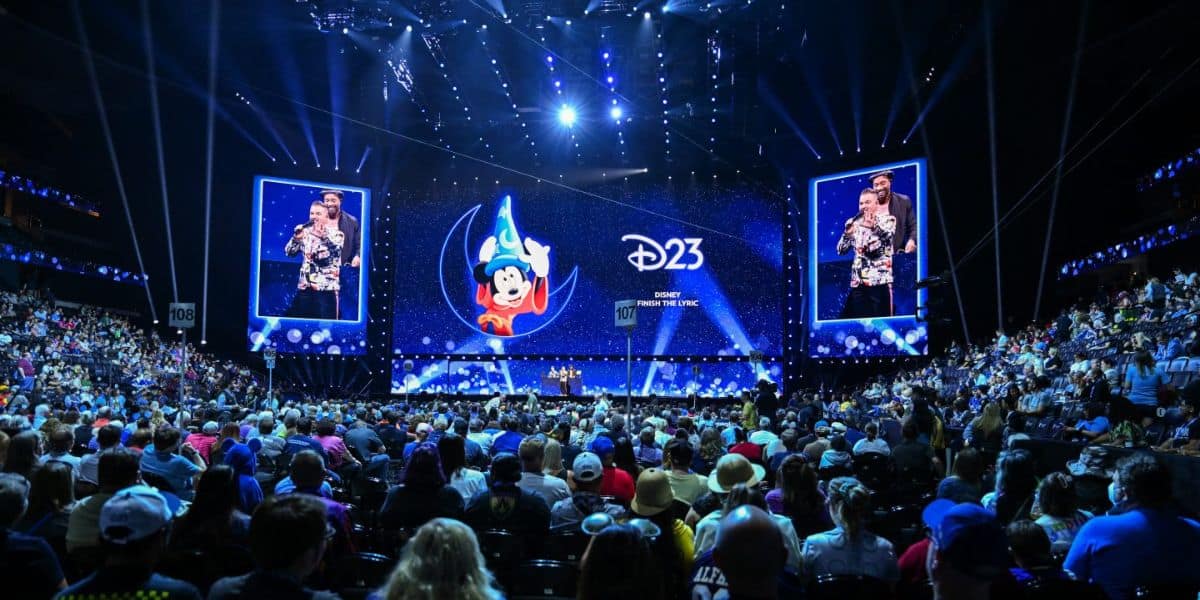 A packed auditorium with blue lighting at D23 with Sorcerer Mickey on the screen