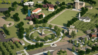 Aerial view of a park with circular pathways, surrounded by trees and grass. There are several buildings, including a church, houses, and a gazebo. Paved walkways and roads connect various areas, and there are open, green spaces throughout.