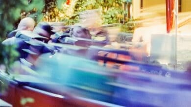 Blurred motion shot of people on a fast-moving amusement park ride, with colorful streaks and greenery in the background. The excitement and speed create a dynamic and energetic atmosphere.