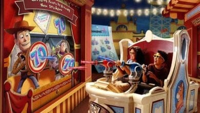 Two people enjoy an interactive ride in an amusement park. They wear 3D glasses and aim at targets with toy guns. The ride features carnival-themed decorations and animated characters on the walls, creating a playful atmosphere.