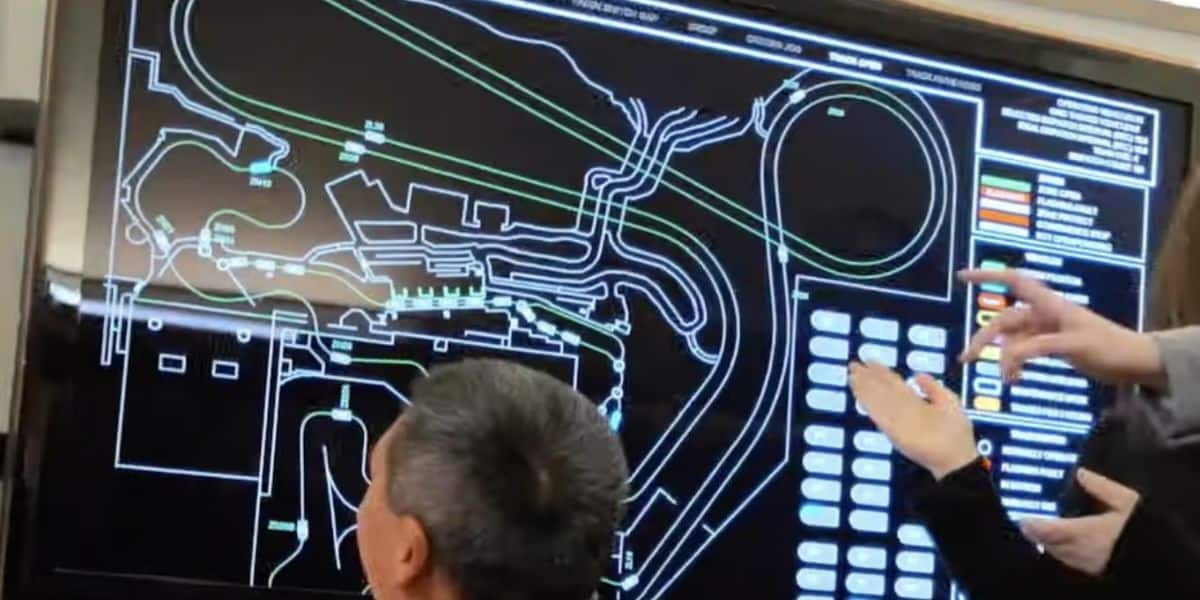People are pointing at a large screen displaying a complex network diagram of Radiator Springs Racers.