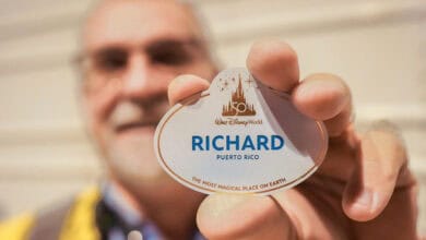 A person holds up a Walt Disney World name tag reading "Richard, Puerto Rico" with "The Most Magical Place on Earth" written below. The person’s face is blurred in the background.