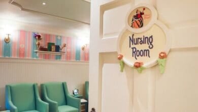 An open door with a sign reading "Nursing Room" reveals a cozy room with teal chairs, pastel-striped wallpaper, and soft lighting.