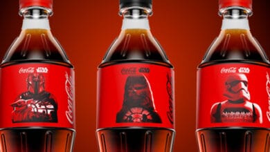 Three Coca-Cola bottles with red labels featuring Star Wars characters: The Mandalorian, Chewbacca, and a Stormtrooper, set against a red gradient background.