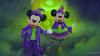 Mickey Mouse and Minnie Mouse wear matching purple and green Halloween costumes with wizard hats at Disneyland.