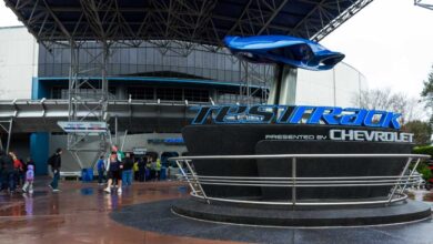 People walk near the entrance to Test Track, an attraction presented by Chevrolet, with a blue car model above the sign at Epcot in Walt Disney World on a rainy day.