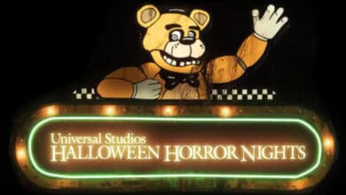 A sign for Halloween Horror Nights at Universal Studios features a large animatronic bear with a bow tie waving above glowing text outlined in neon lights.