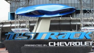 A large outdoor Test Track sign with a blue futuristic car shape on top, and "Presented by Chevrolet" written beneath. Metal supports and a building are visible in the background.