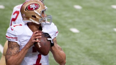 A football player in a San Francisco 49ers uniform holds a football, preparing to throw a pass during a game.