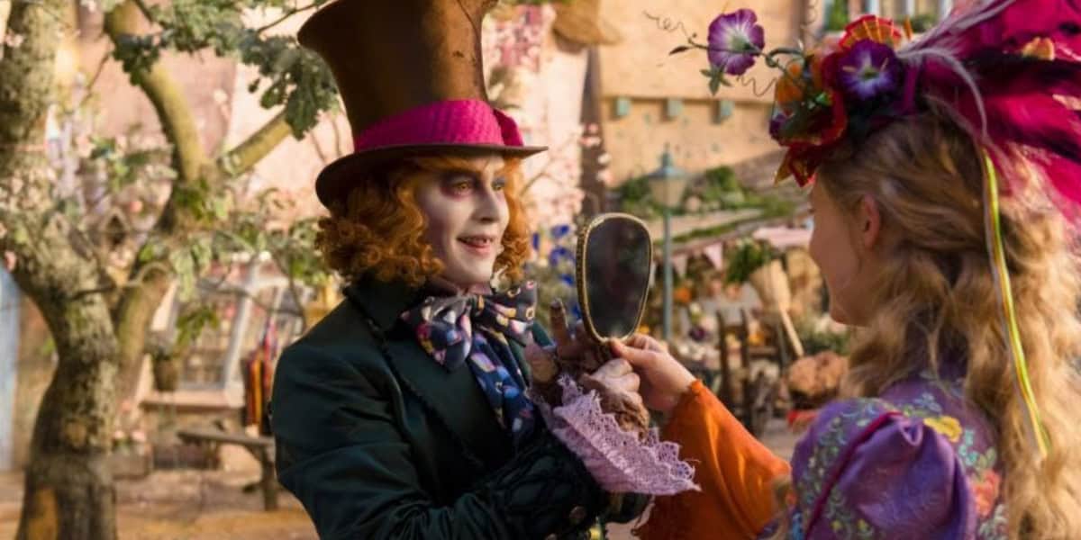 A man in a tall hat and colorful clothes smiles while holding a mirror, facing a woman in a vibrant, flower-adorned outfit. Their whimsical, colorful setting feels straight out of one of the most enchanting sequels.