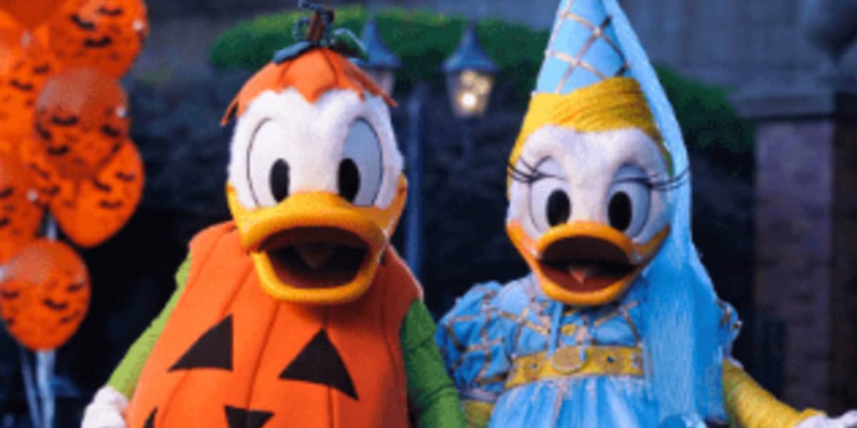 Donald Duck dressed as a jack-o'-lantern and Daisy Duck as a princess stand side by side outdoors, with orange Halloween party balloons in the background.