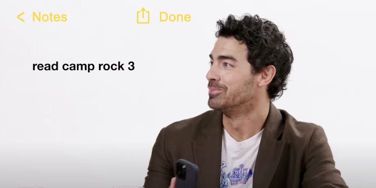 A man with dark curly hair and a beard holds a phone, looking to his left. On the screen, text reads "read camp rock 3" in a Notes app interface with yellow icons for Notes and Done.