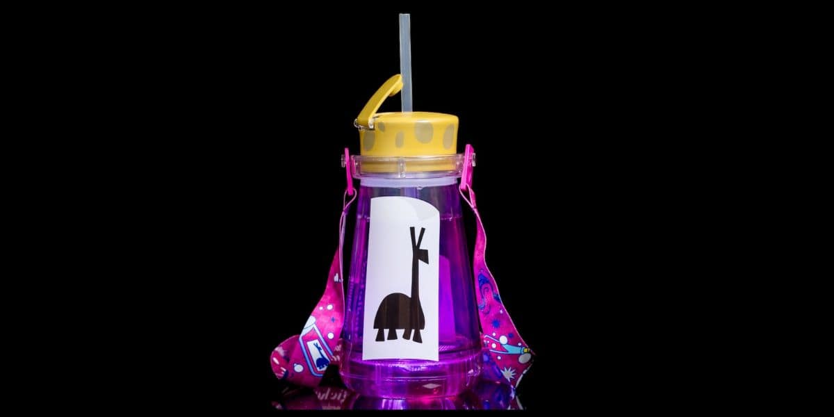 A purple sipper water bottle with a yellow lid, clear straw, and pink strap. A black animal silhouette is printed on a white sticker on the bottle. The background is black.