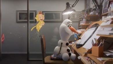 A 3D animated snowman sits at a cluttered desk drawing, while a glowing, cartoon lion cub with fairy wings floats nearby. The scene appears to blend animation styles in a creative workspace.
