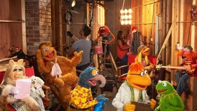 The Muppets characters, including Miss Piggy, Fozzie Bear, Gonzo, and Kermit, bustle backstage on a lively set as they prepare for a show—just like you’ll find on The Muppets Disney Plus series.