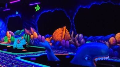 A glowing, underwater-themed mini-golf course with neon blue whales, colorful sea creatures, and vibrant coral decorations under blacklights.