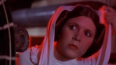 A woman with brown hair styled in two side buns, wearing a white outfit and hood, looks intently to the side under red-tinted lighting.