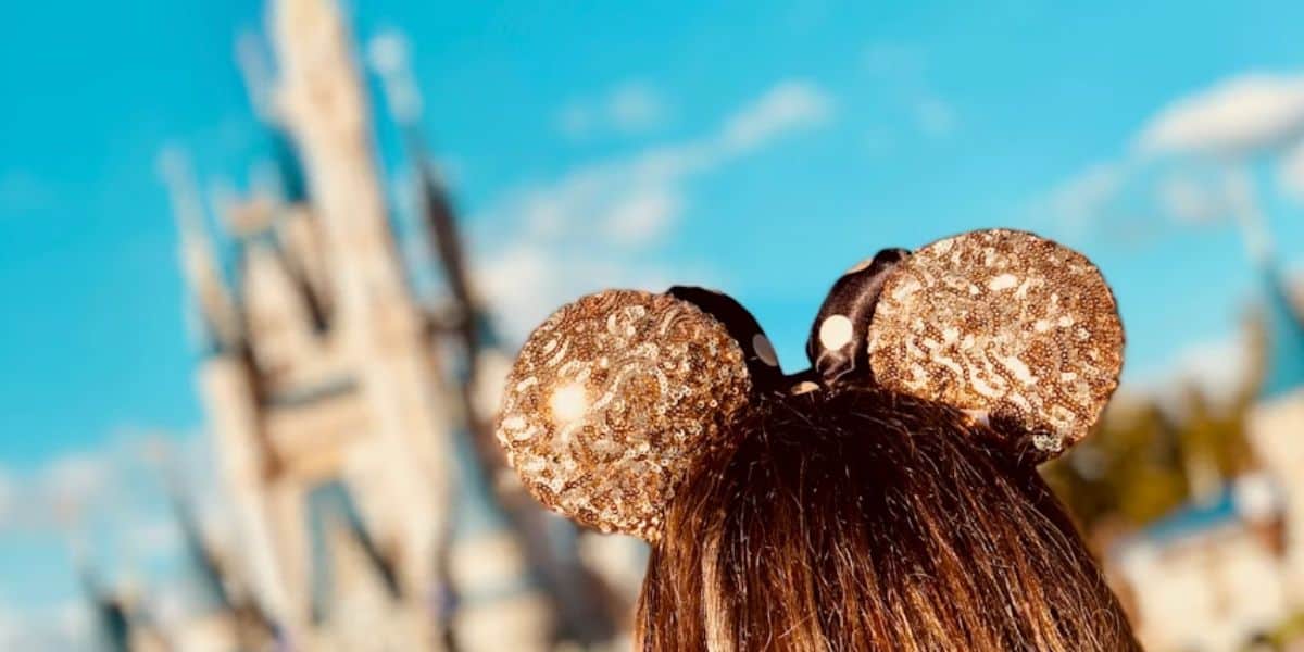 guest wearing gold mickey ears in front of disney world's cinderella castle in magic kingdom