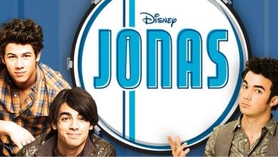 Three young men, the Jonas Brothers, pose in front of a large drum with the Disney “JONAS” logo. The blue background with white stripes adds energy as they smile in their casual clothes.