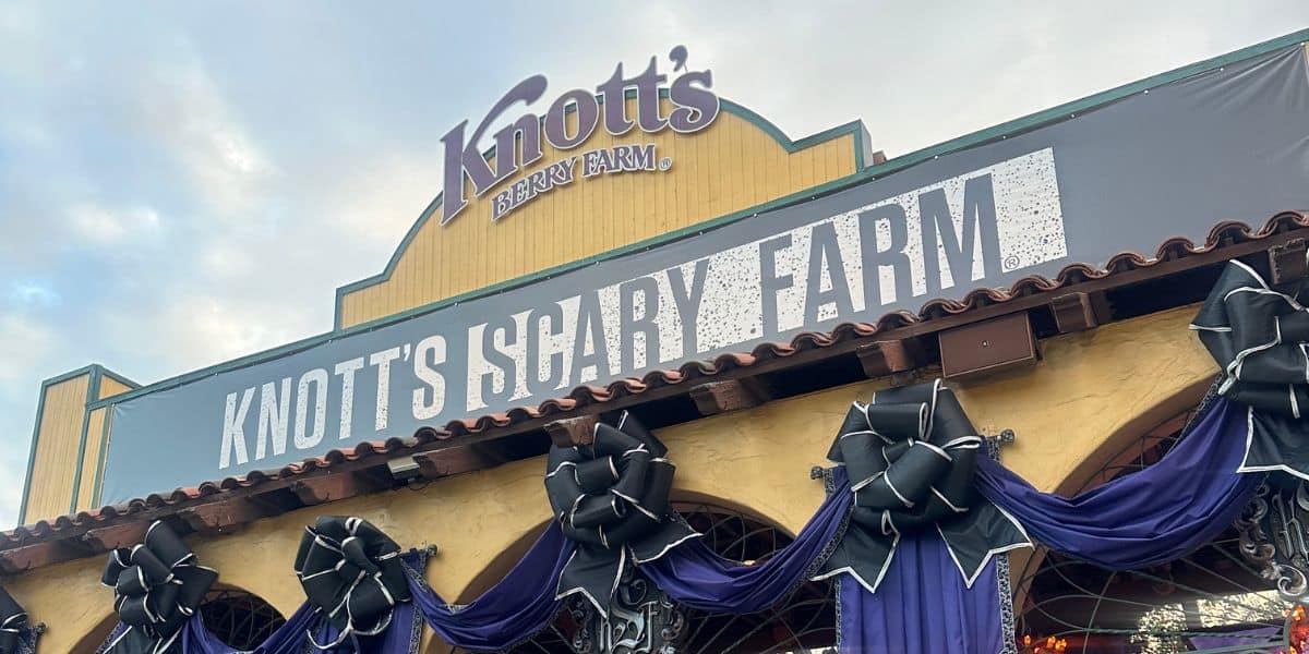 The entrance to Knott’s Berry Farm decorated for Knott’s Scary Farm, with a large sign, black bows, and draped purple fabric. The Knott's Berry Farm logo is visible above the event banner.