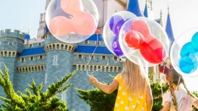 two kids hold Mickey Mouse balloons in front of Cinderella Castle in Disney World's Magic Kingdom park