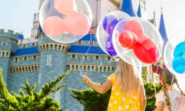 two kids hold Mickey Mouse balloons in front of Cinderella Castle in Disney World's Magic Kingdom park