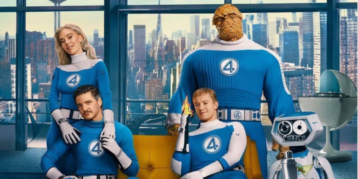 Four people in blue Fantastic Four costumes pose in a modern room with large windows showing a city skyline. One is a rocky orange figure, one is holding a flame, and a small robot is beside them.