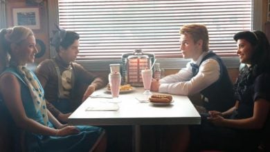 Four teenagers sit in a retro diner booth, two on each side, with milkshakes and food on the table. The setting features a jukebox and blinds with sunlight streaming through.
